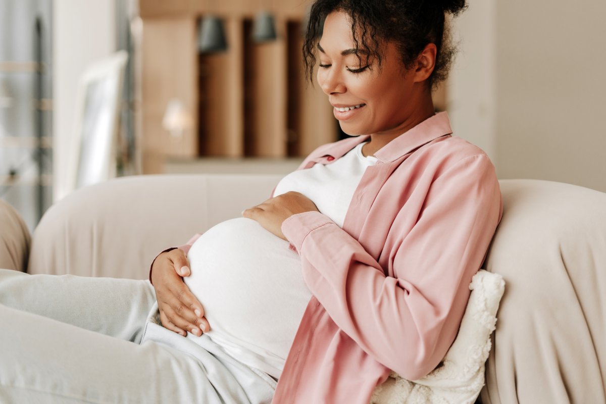 A pregnant woman sitting with her hands on her belly.