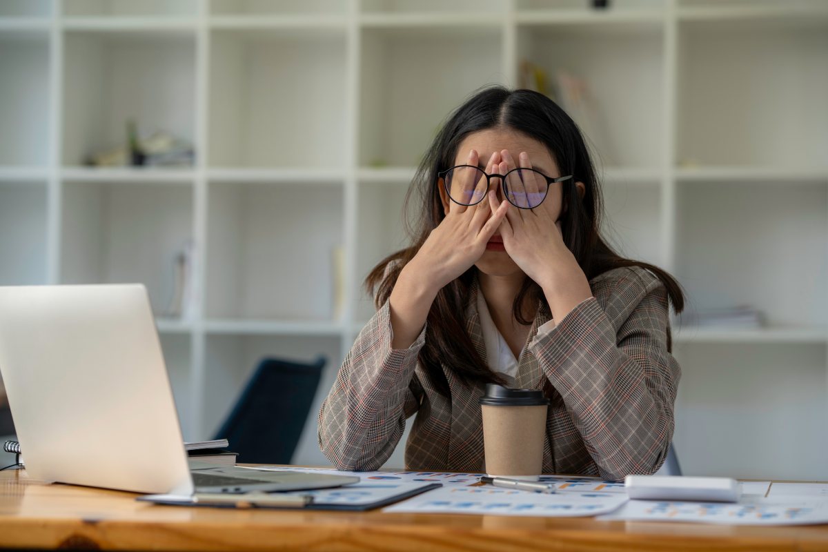 A stressed woman sitting at a desk with her head in her hands.